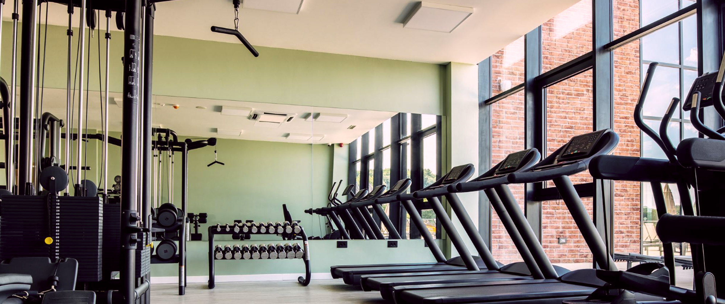 На картинке изображен светлый, современный спортивный зал, с новыми тренажёрами, беговыми дорожками, большими зеркалами и окнами